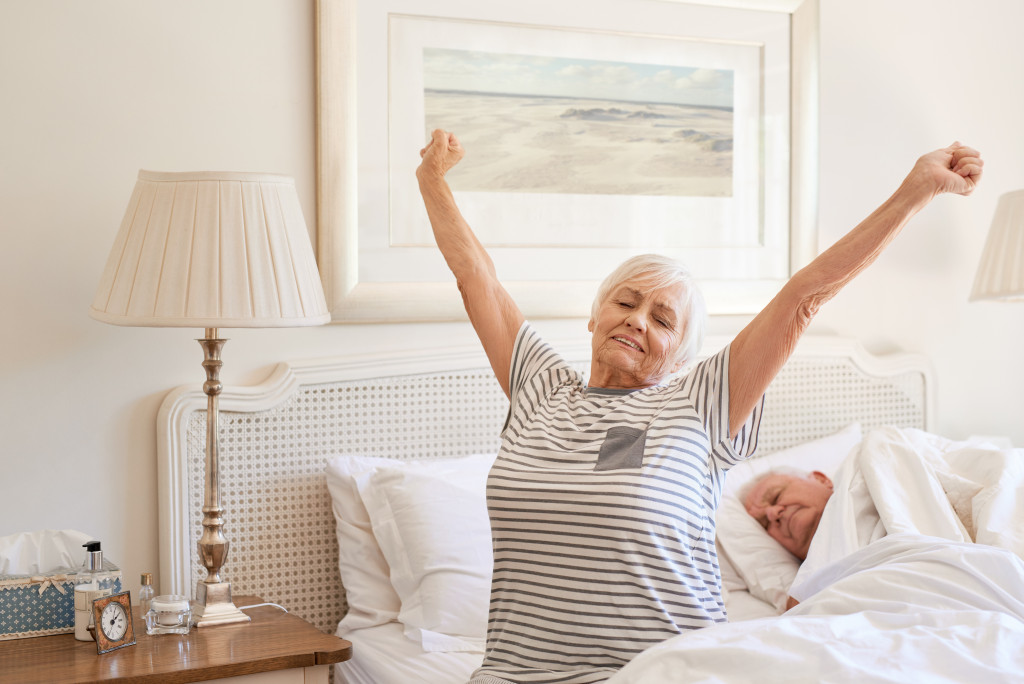 An elderly woman yawning beside her sleeping husband in bed