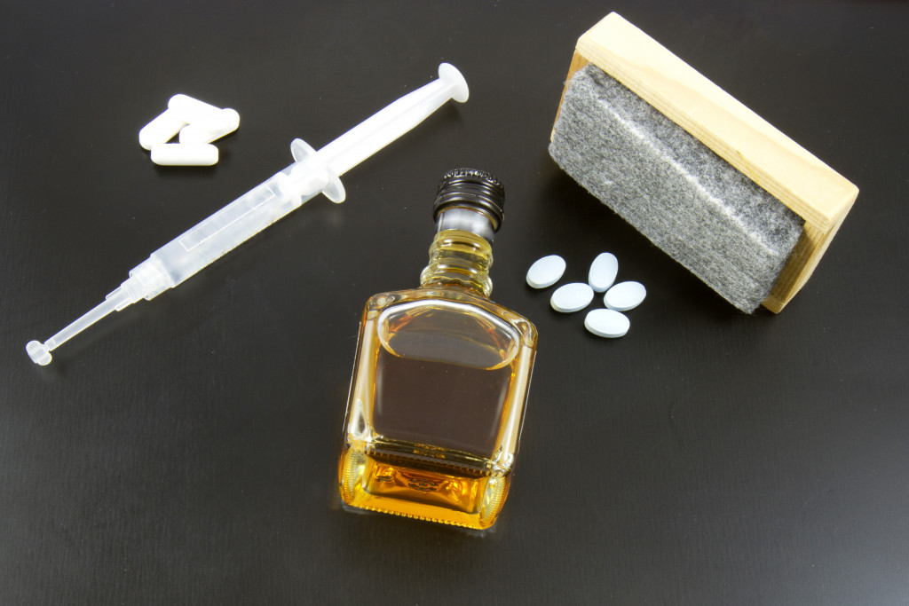 alcohol, pills, and syringe on blackboard with eraser