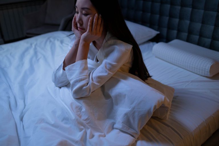 Woman in White Long Sleeve Shirt Sitting on a Bed