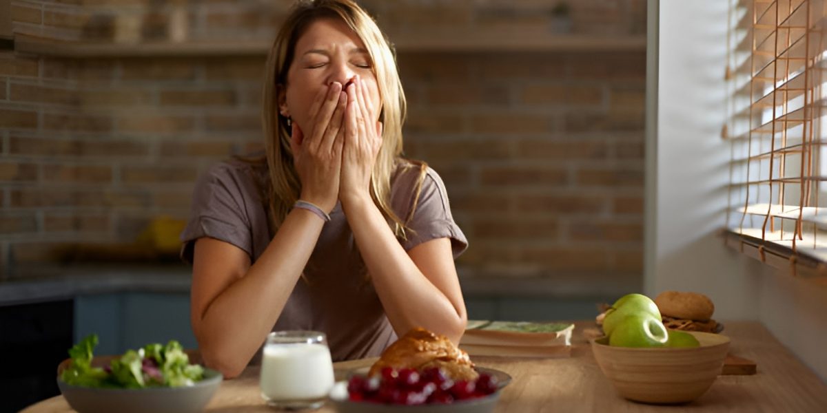 woman yawning, resting elbows on a table with food and milk