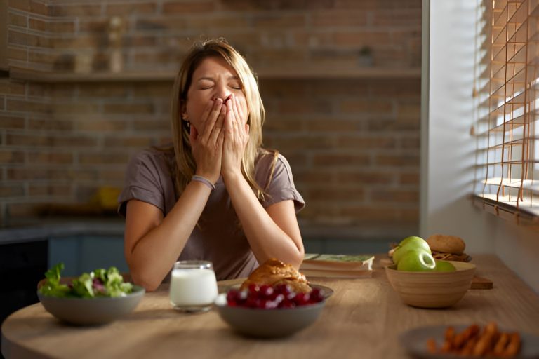 woman yawning, resting elbows on a table with food and milk