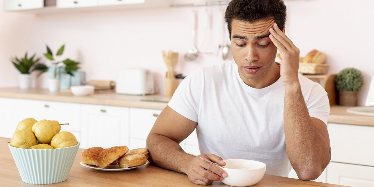 sleepy man sitting in a kitchen, looking down into a bowl