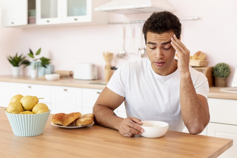 sleepy man sitting in a kitchen, looking down into a bowl