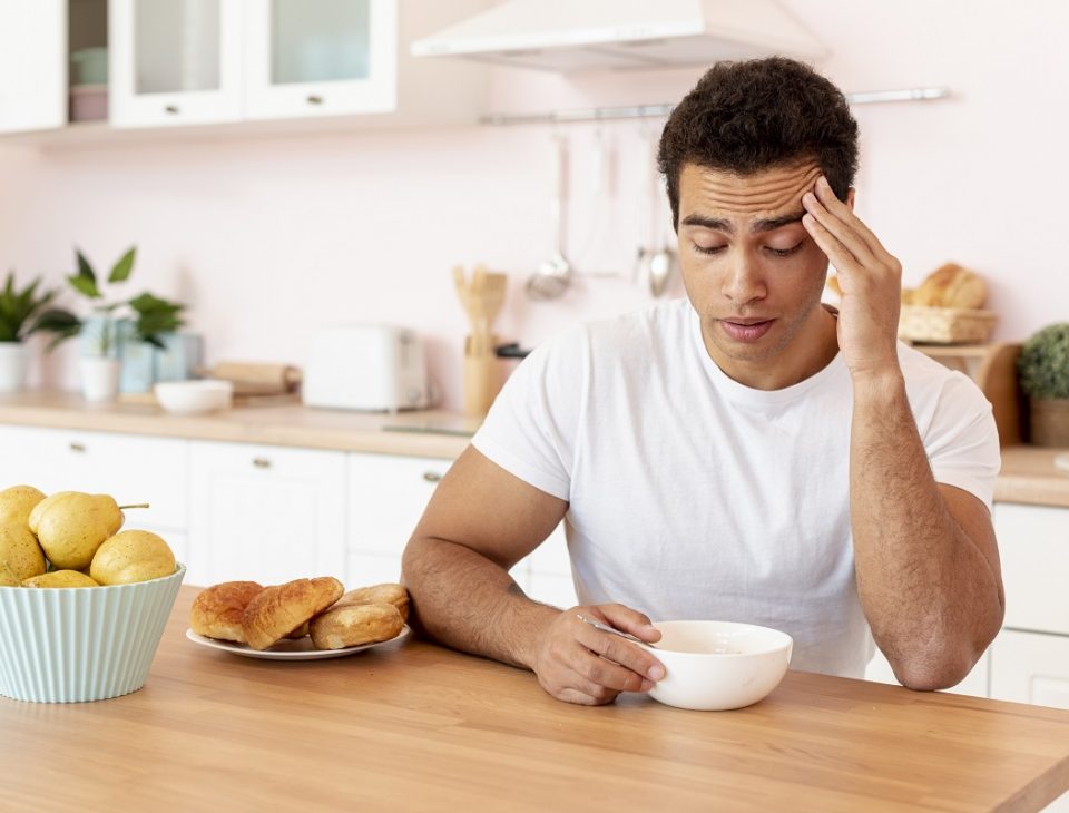sleepy man sitting in a kitchen, looking down into a bowl